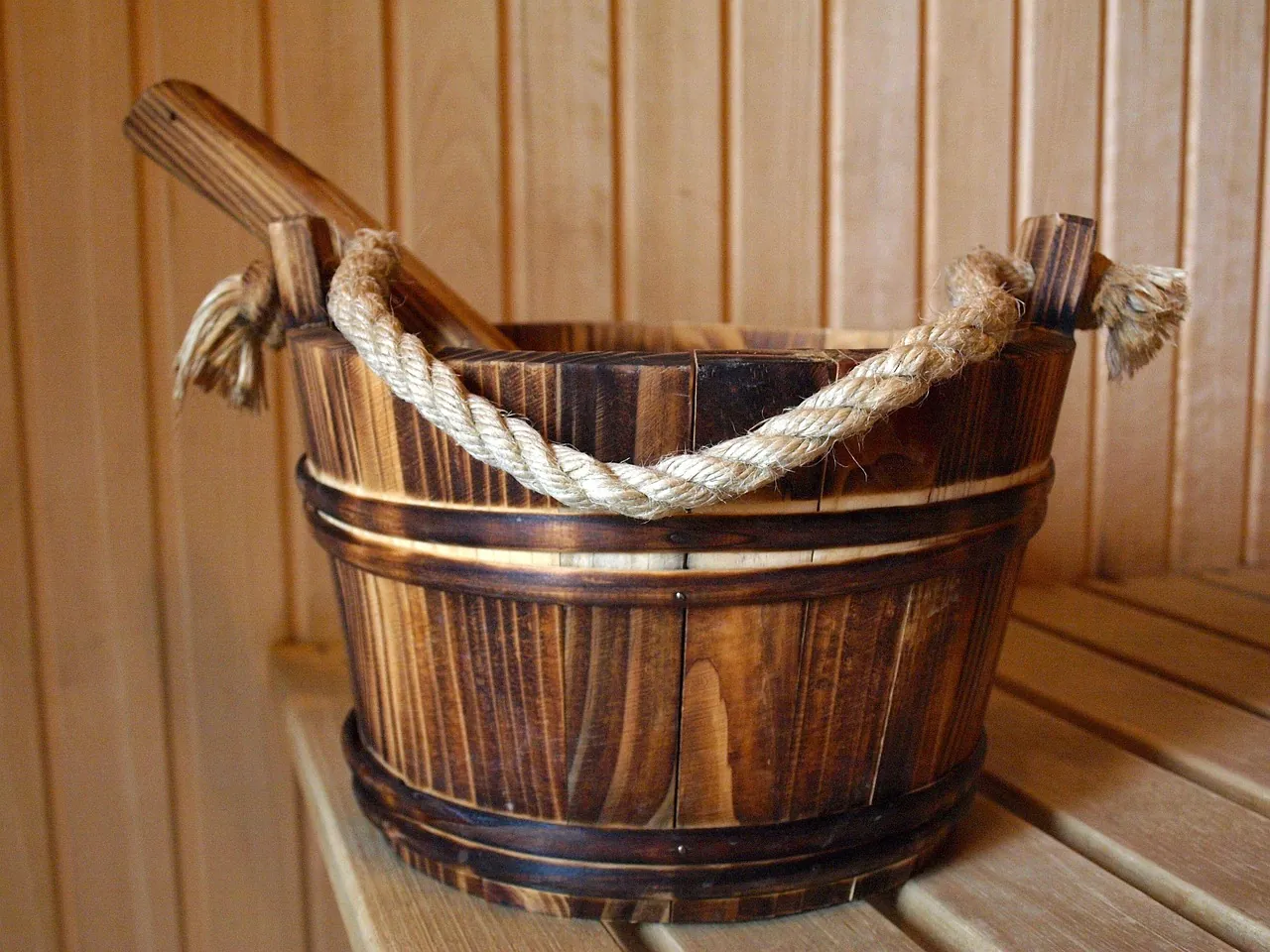 A rustic wooden sauna bucket and ladle sitting on a wooden bench inside a sauna
