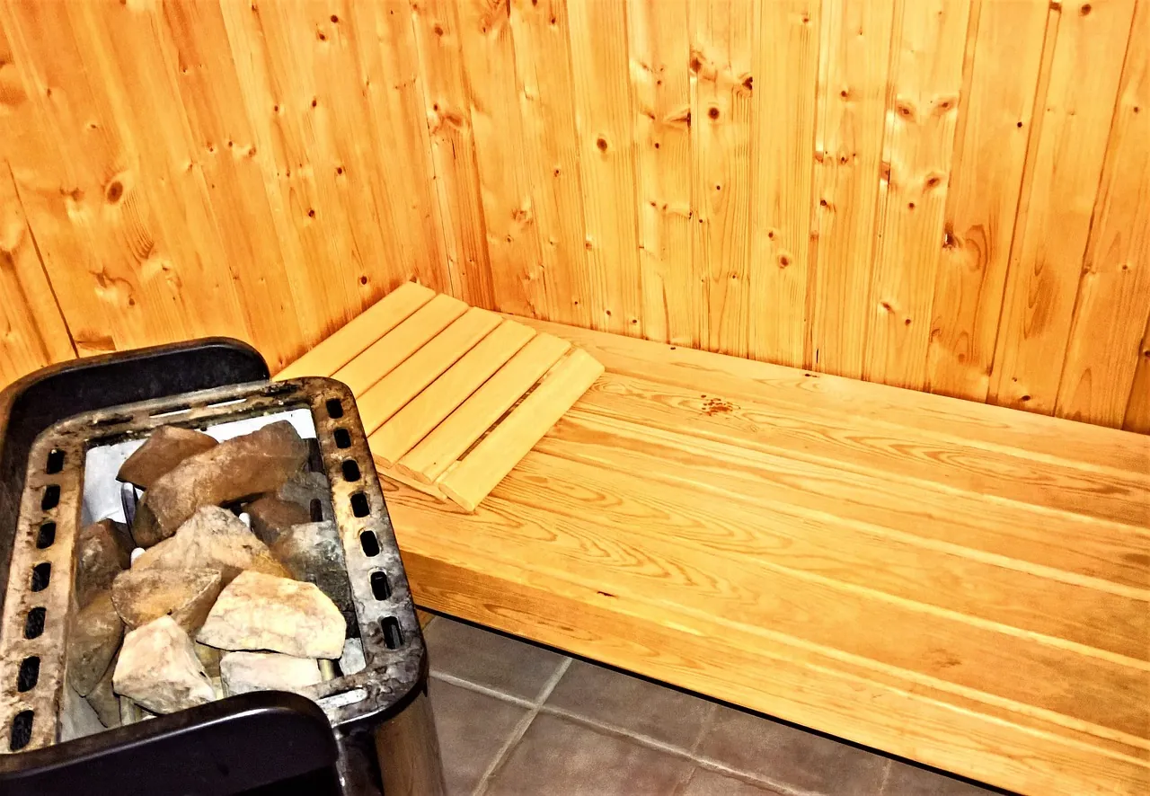 A traditional sauna heater filled with rocks beside a wooden bench in a pine-paneled sauna room