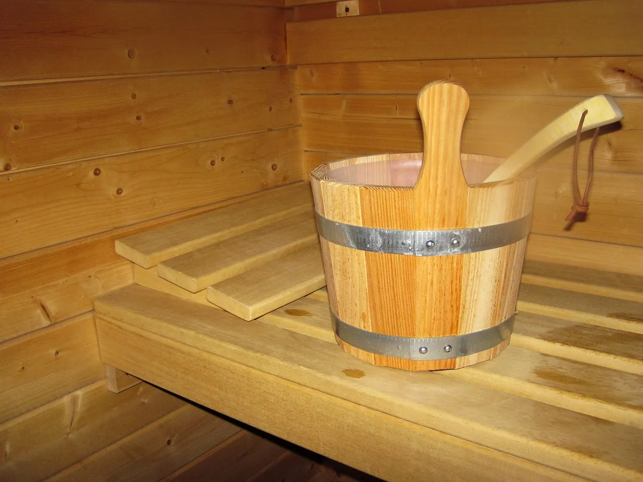 A wooden sauna bucket and ladle resting on a slatted bench inside a pine sauna room